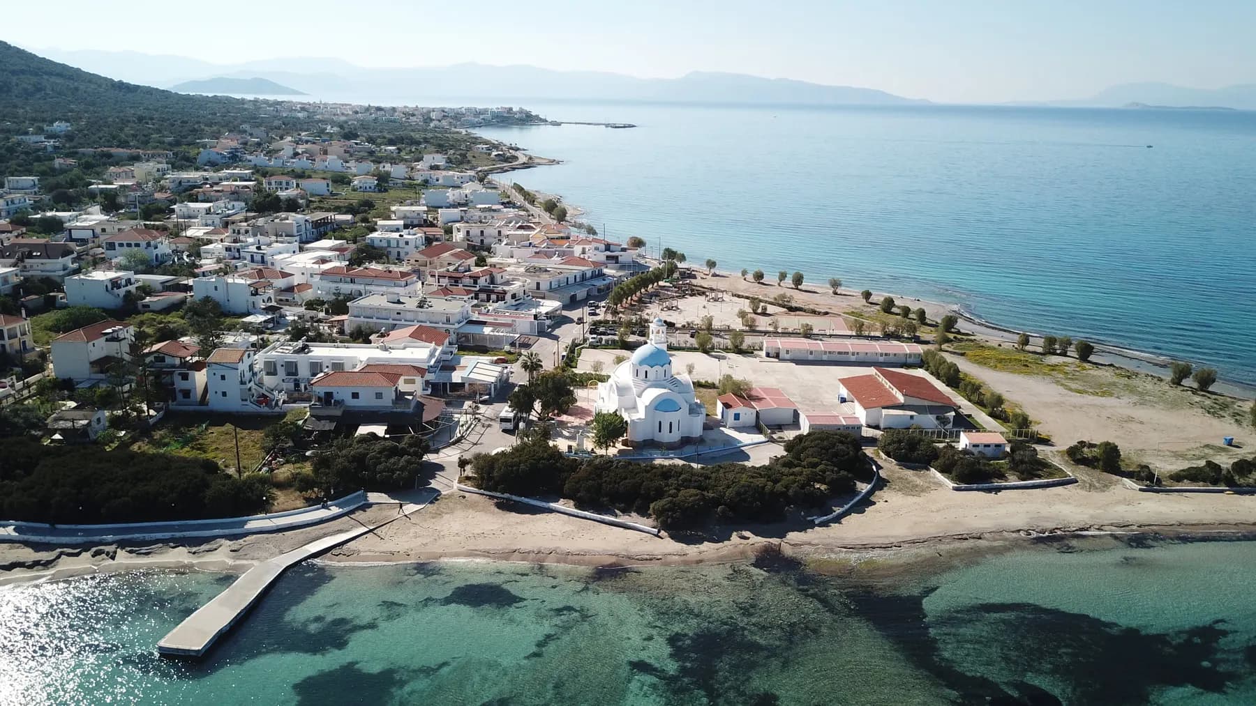Aerial view of Agistri's seafront village, its blue-domed church, and sandy beach