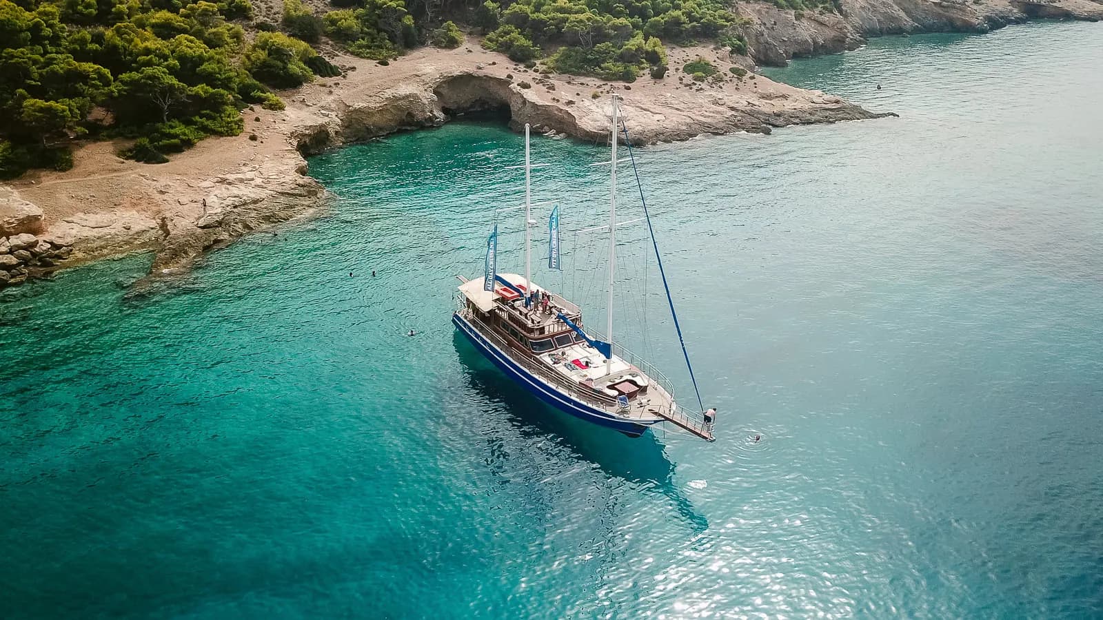 The boat anchored beside a rocky cove with a sea cave, swimmers nearby