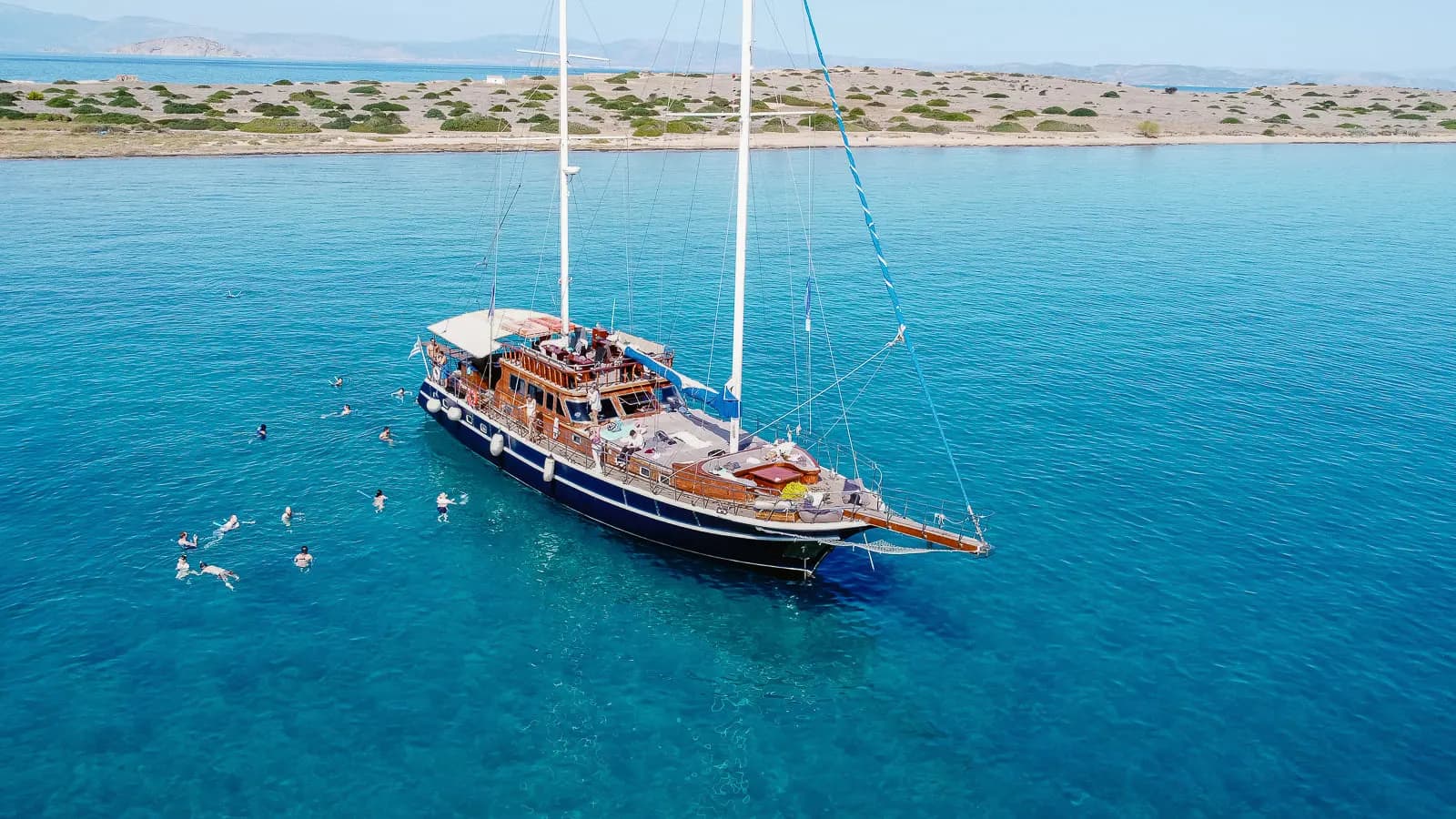 Guests swimming around the anchored boat near a sandy shoreline