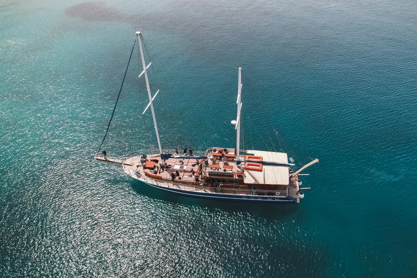 Aerial view of the boat at anchor in open water, guests relaxing on deck