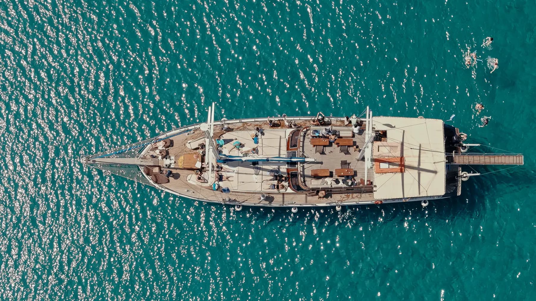 Aerial view of guests on deck with swimmers alongside in turquoise water